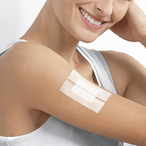 Woman smiling with Leukosilk (Hypoallergenic) Tape applied on her upper arm, showing breathable medical tape use.